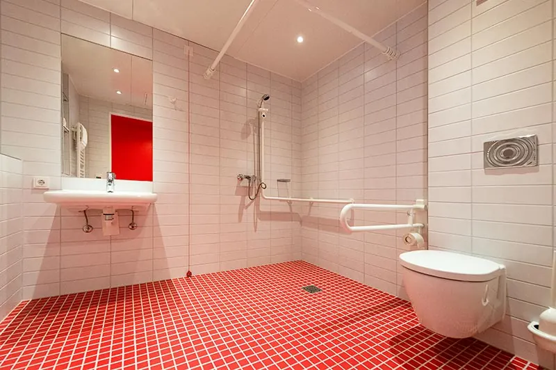 Barrierefreies Bad mit bodengleicher Dusche, Haltegriffen und rotem Fliesenboden